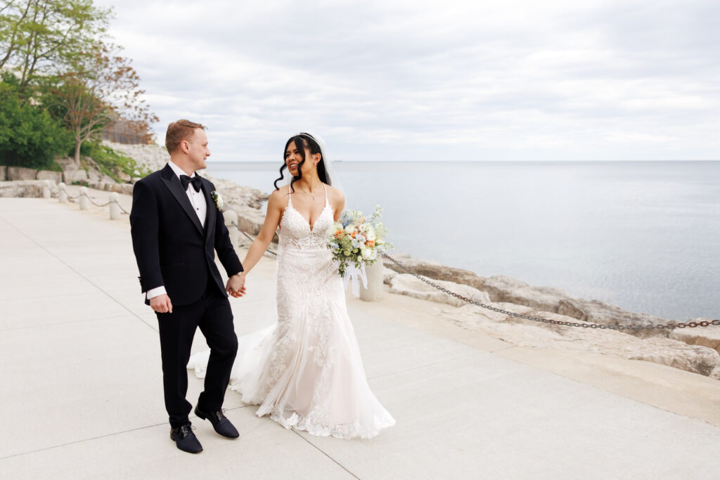Bride and groom walking hand-in-hand along Burlington waterfront at The Pearle Hotel.
