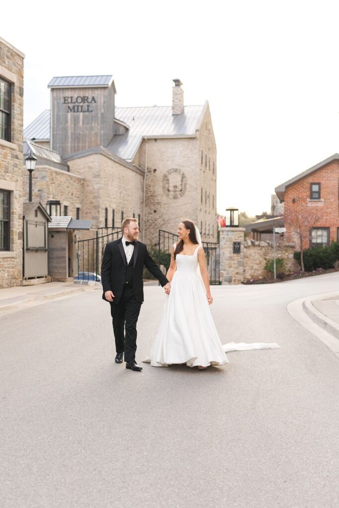 bride and groom walking in the street in front of elora mill